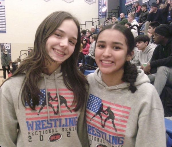 Lily Blasius (left) and Osmairi Medina Alvarado (right) smiling for the camera at a girls wrestling meet.